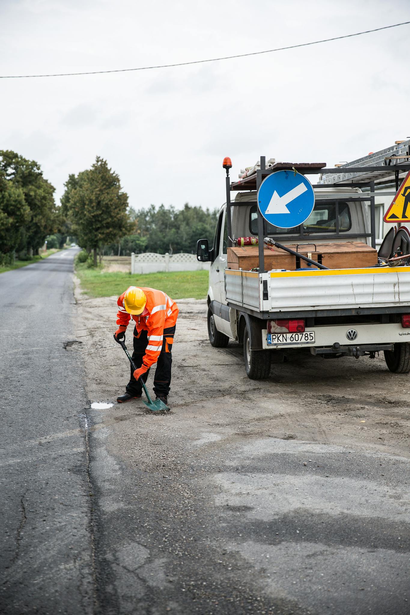 A road maintenance worker fixes a pothole next to a truck in a rural setting.