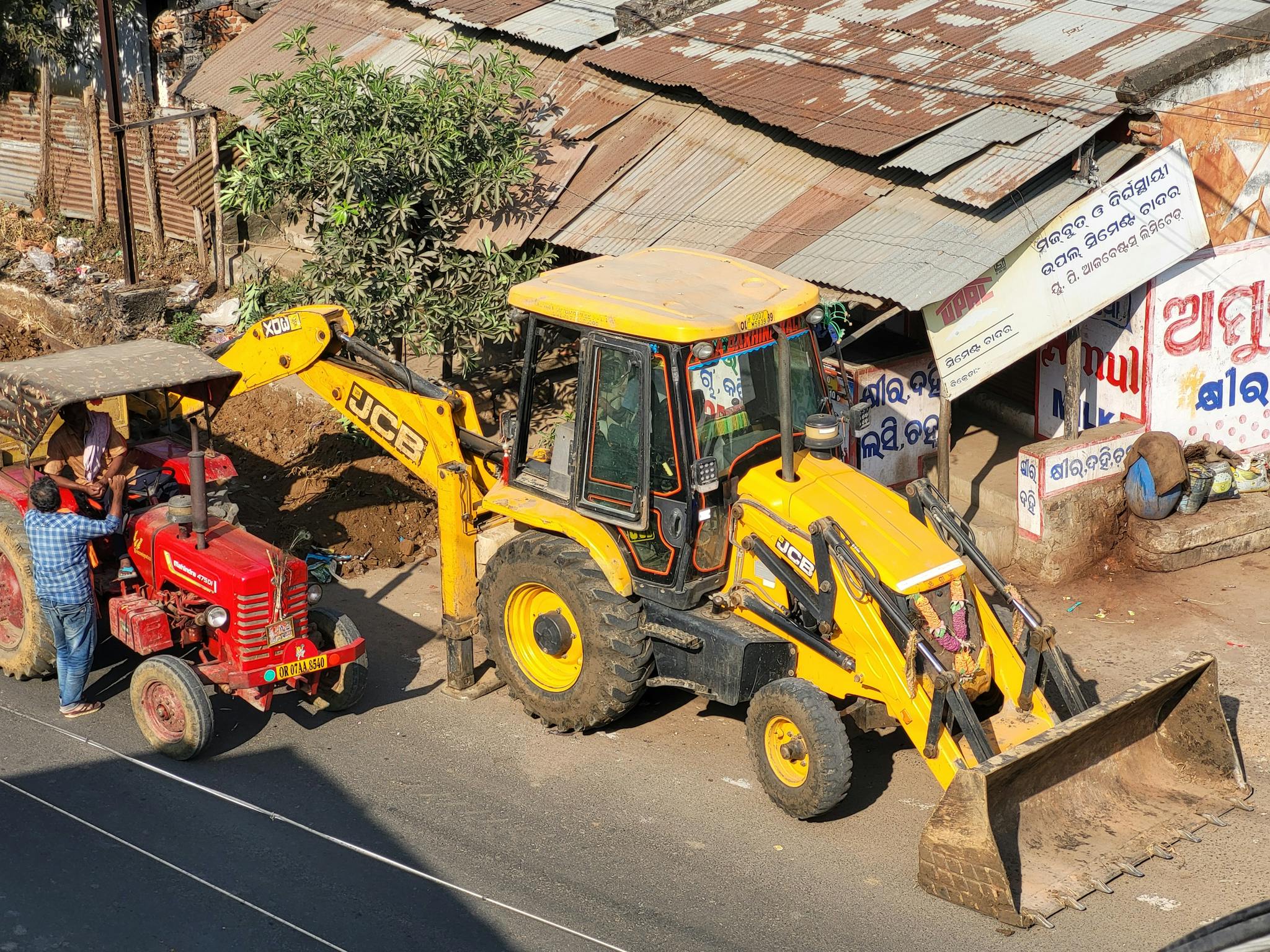 JCB backhoe and a red tractor working at roadside construction with rustic background.